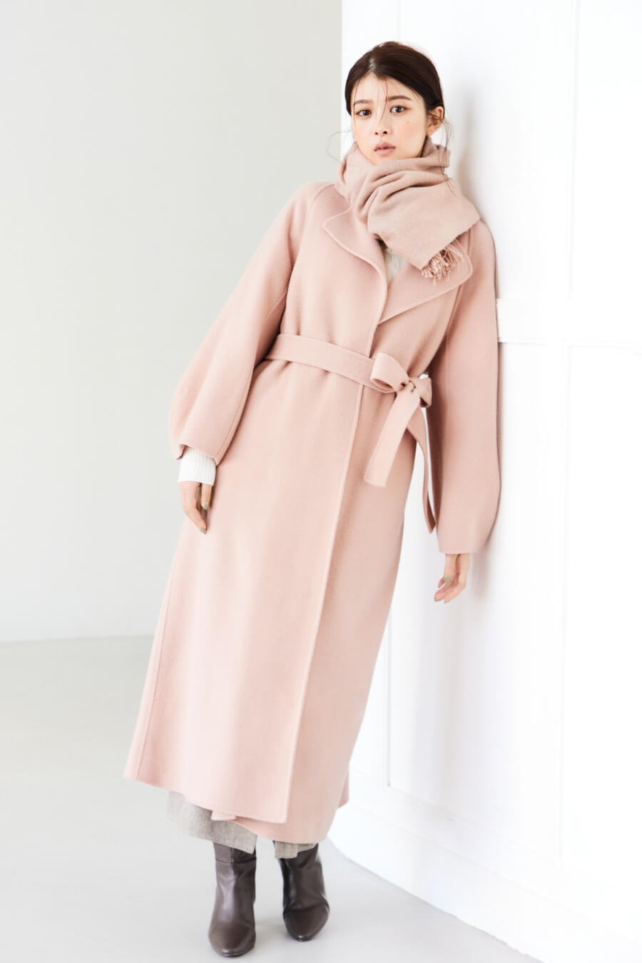 ライトピンクのコート・アイボリーのニット・ベージュのパンツを履いた女性