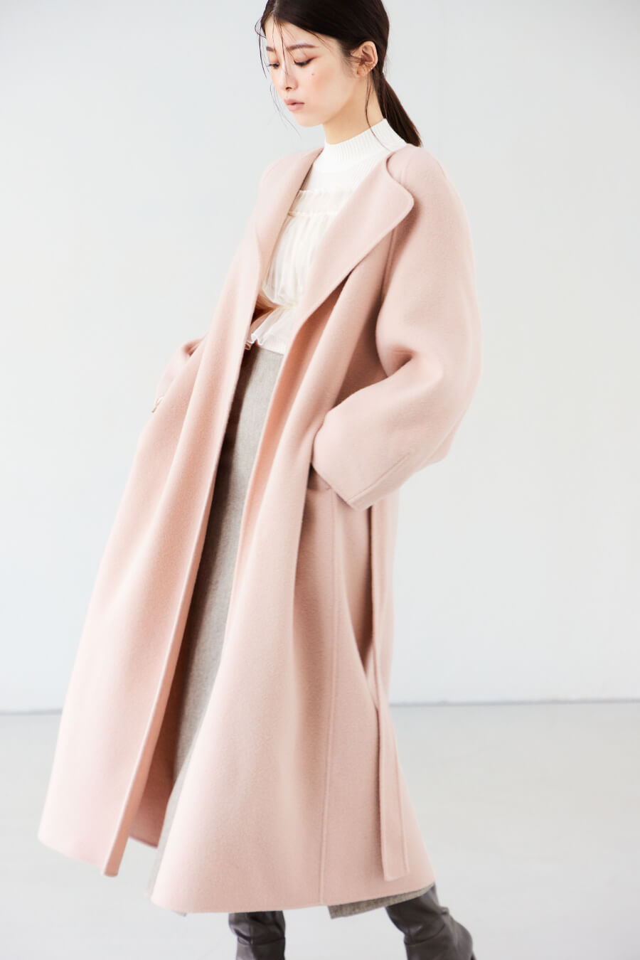 ライトピンクのコート・アイボリーのニット・ベージュのパンツを履いた女性